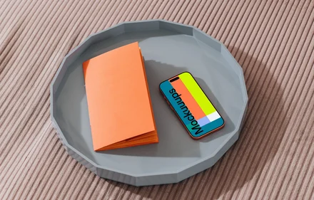 iPhone 17 Pro mockup on a gray tray with an orange notebook